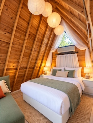 Una stanza di legno accogliente dalla forma triangolare, con un letto, comodini e una finestra con tende.