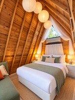 A cozy, triangular wooden room with a bed, nightstands, and a window with curtains.