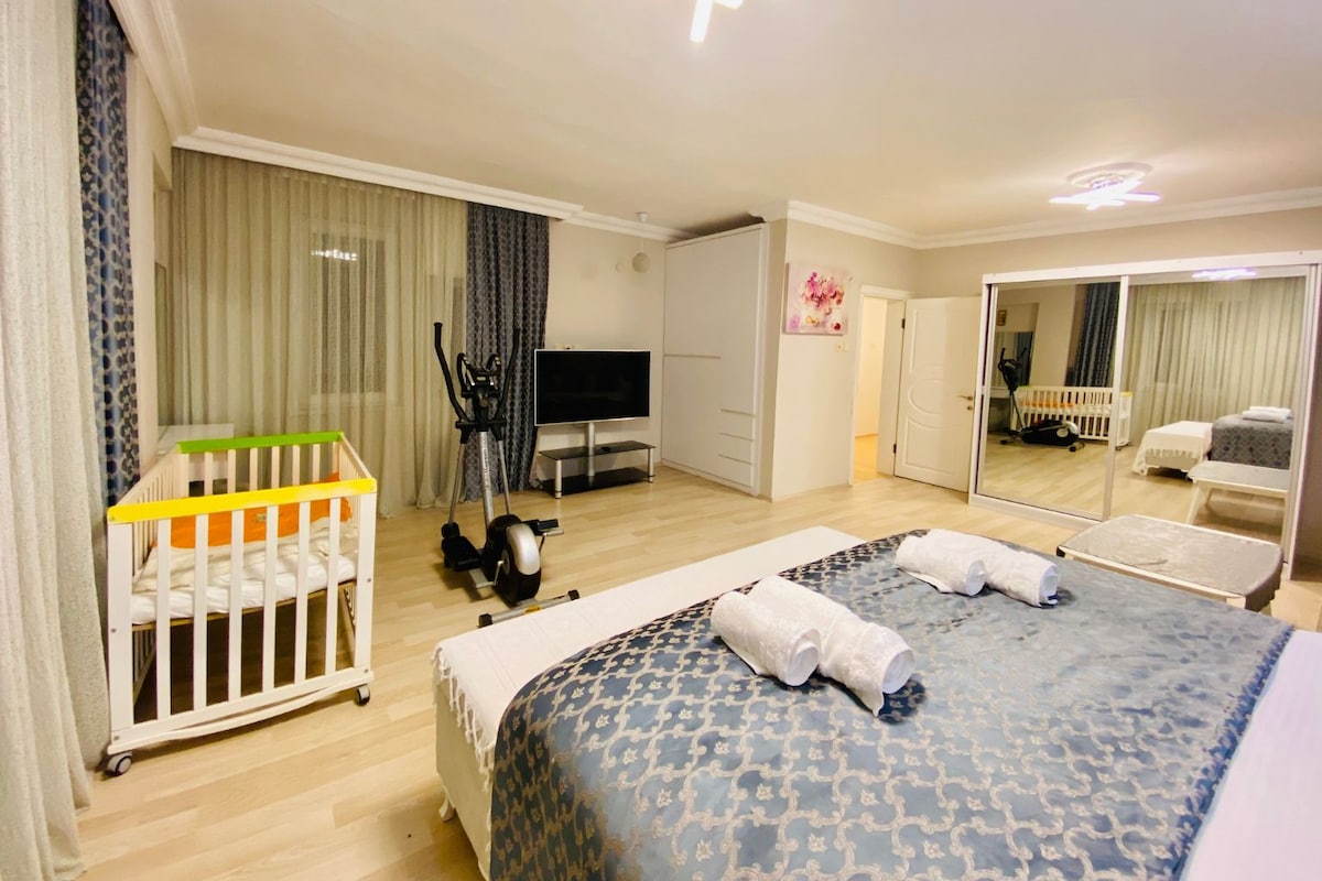 Una camera d'albergo con un letto, una culla, una televisione, uno specchio e una porta che dà su un'altra stanza.
