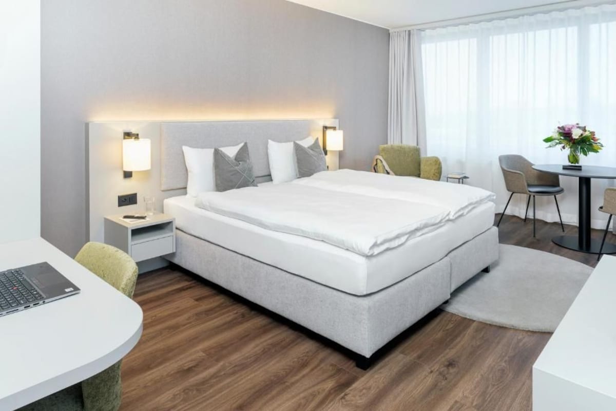 A modern hotel room with a large bed, bedside tables, a desk, and a chair.