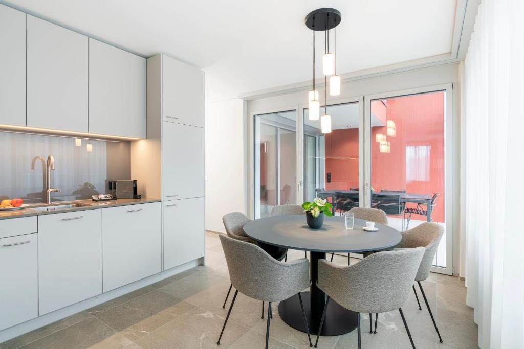 Una cocina moderna con armarios blancos, una mesa redonda con sillas e iluminación colgante.