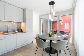 A modern kitchen with white cabinets, a round dining table with chairs, and a pendant light. - CITY STAY - Papieri-Ring (Cham)