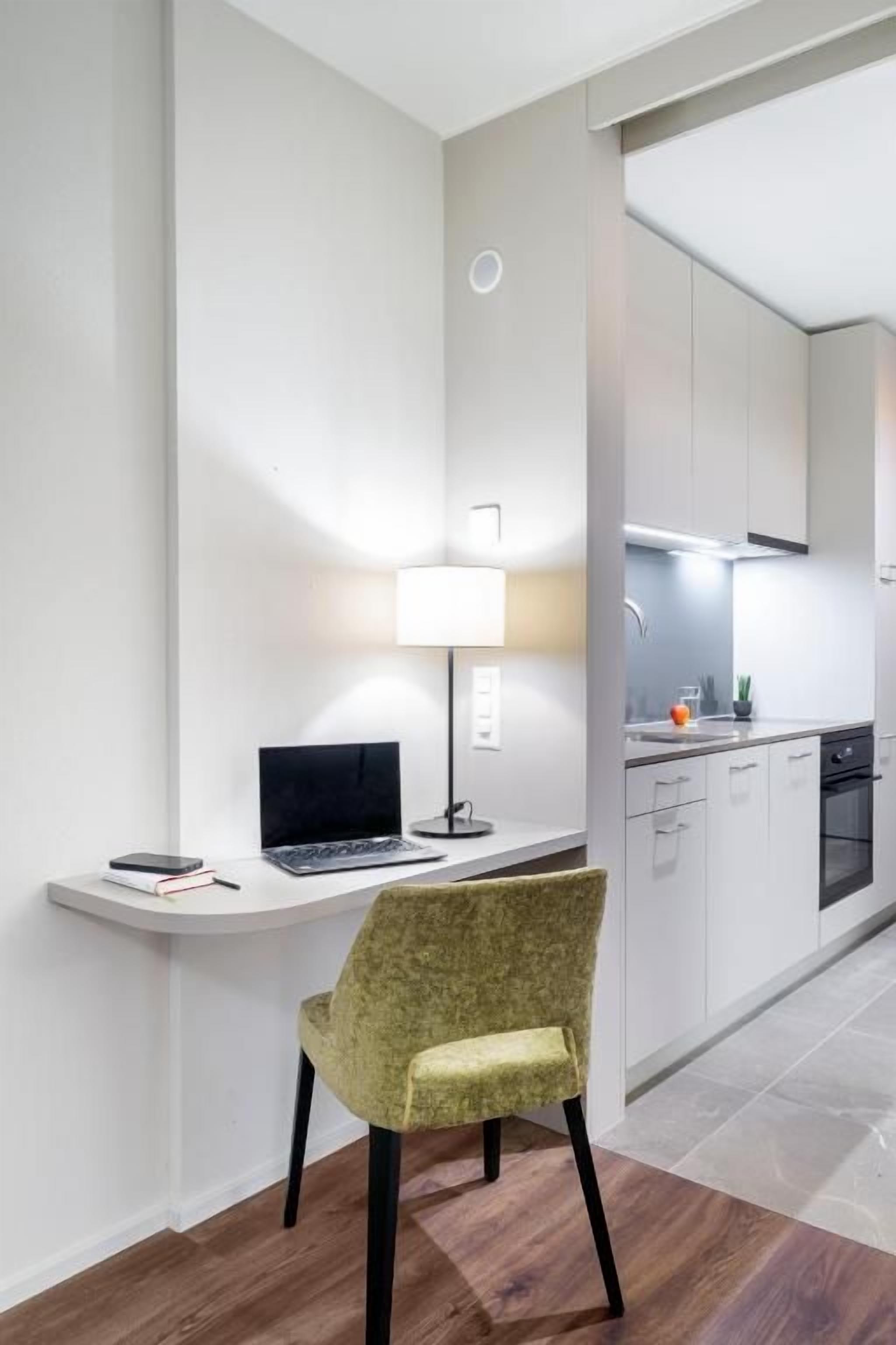 A modern kitchen with white cabinets, a built-in oven, and a countertop with a kettle and a fruit bowl.