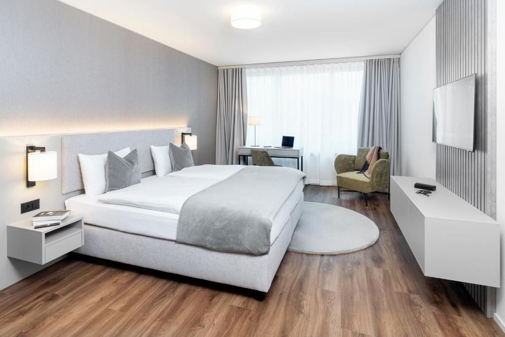 A modern hotel room with a large bed, bedside tables, a desk, a chair, a TV, and a round rug.