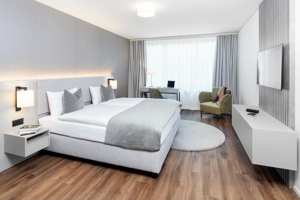 Una habitación de hotel moderna con una cama grande, mesitas de noche, un escritorio, una silla, un televisor y una alfombra redonda.