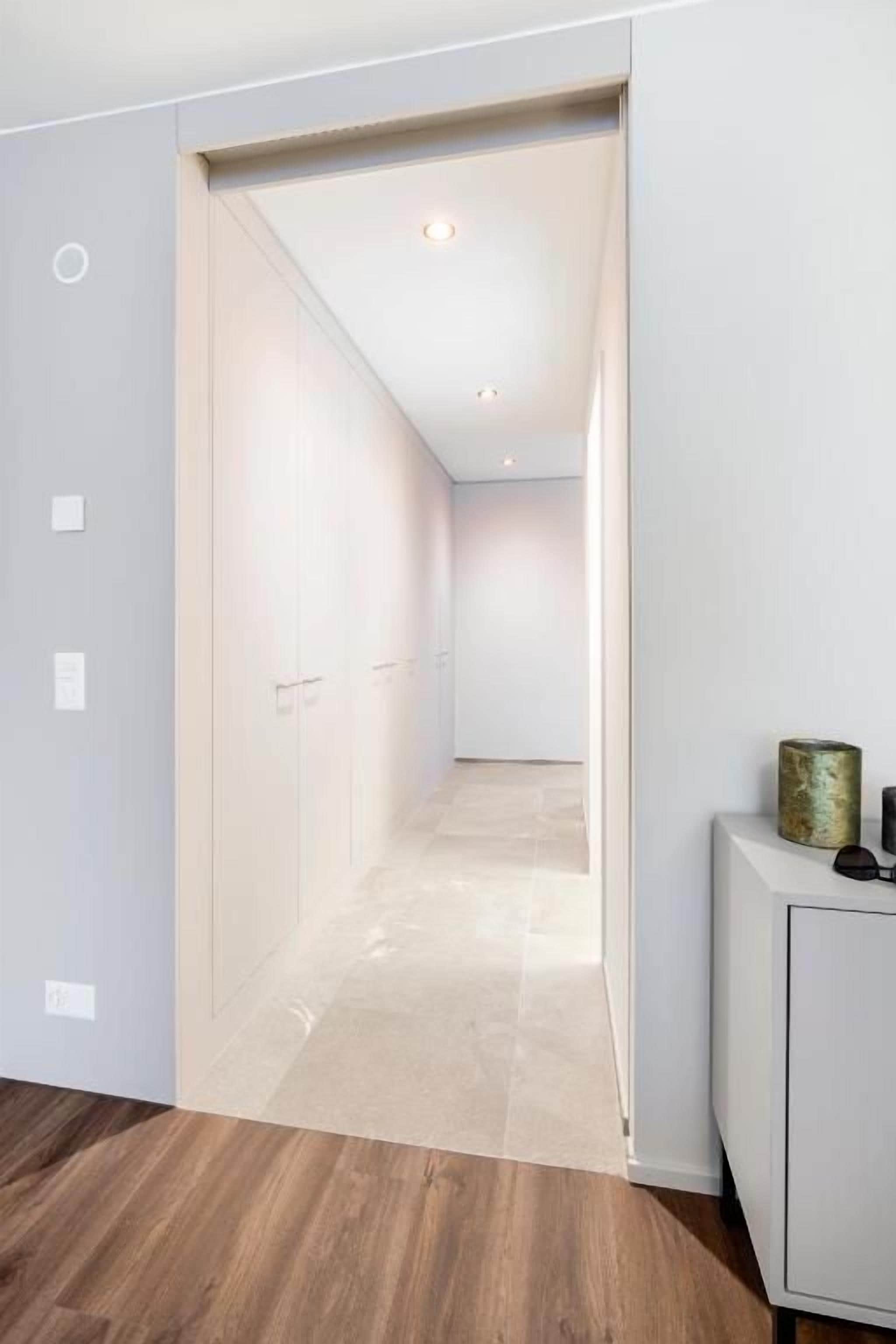 Un pasillo con piso de madera, un armario blanco y una puerta que da a otra habitación.