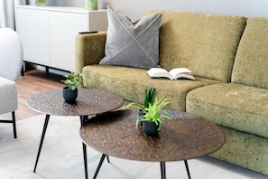A modern living room with a green sofa, two round tables with potted plants, and an open book on the sofa. - CITY STAY - Papieri-Ring (Cham)