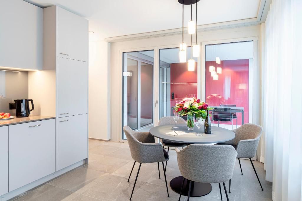 A modern kitchen with white cabinetry, a dining area with a round table and grey chairs, and a large window with a red interior view.