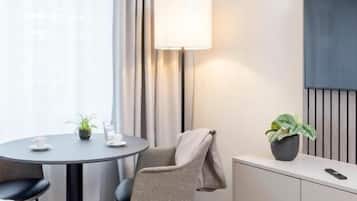 Habitación de hotel con una cama, un escritorio con lámpara, una silla, una planta en maceta y un televisor sobre un pedestal.