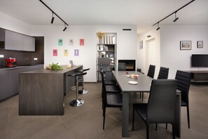 A modern kitchen with a central island, dining table with chairs, and a TV mounted on the wall. - New Listing (Krnica)