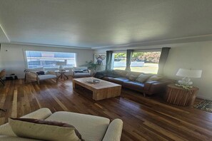 Ein geräumiges Wohnzimmer mit Holzboden, einem großen Fenster und einer gemütlichen Sitzecke mit Sofa und Sesseln.
