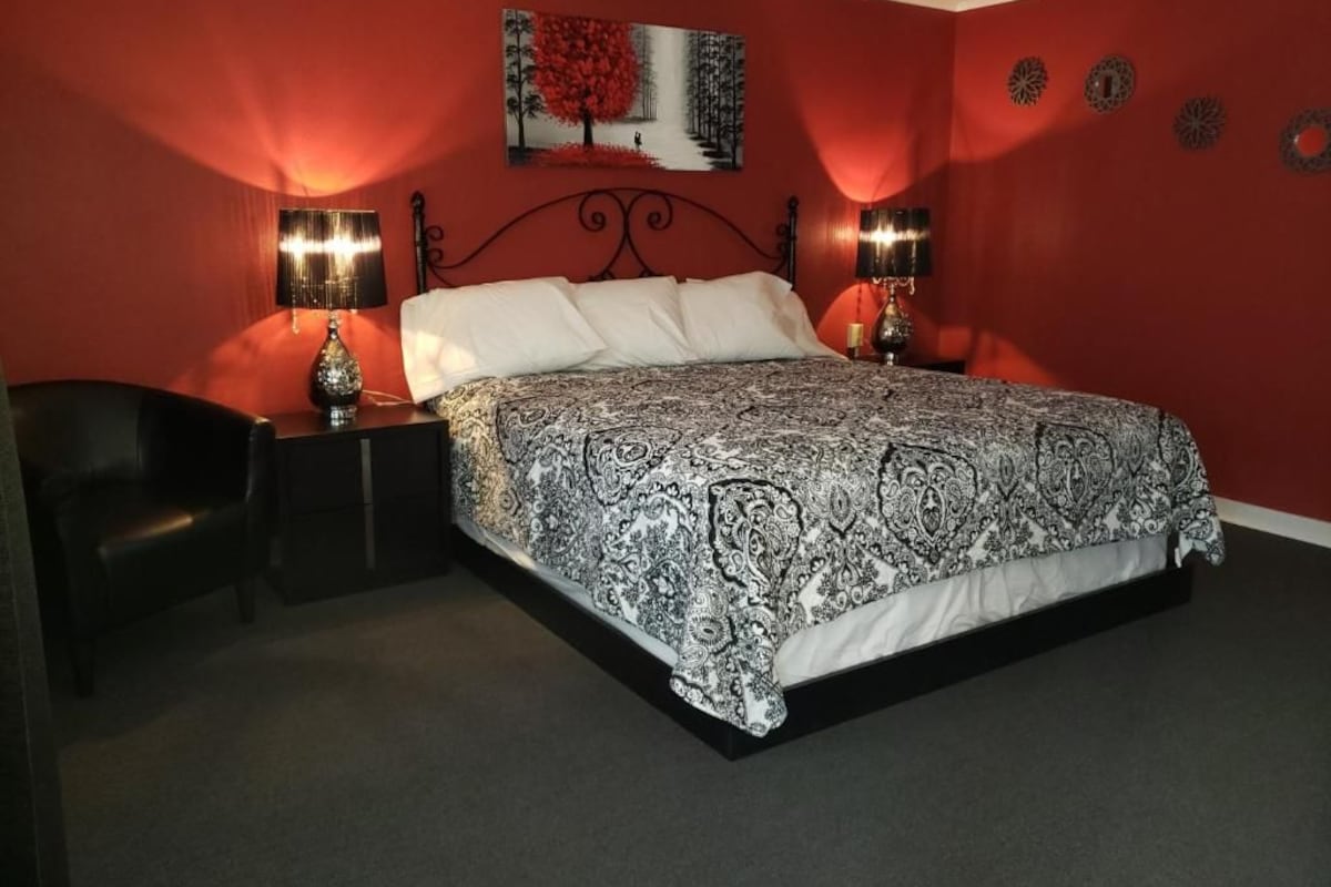 A bedroom with a large bed, two bedside lamps, a chair, and a wall-mounted artwork.