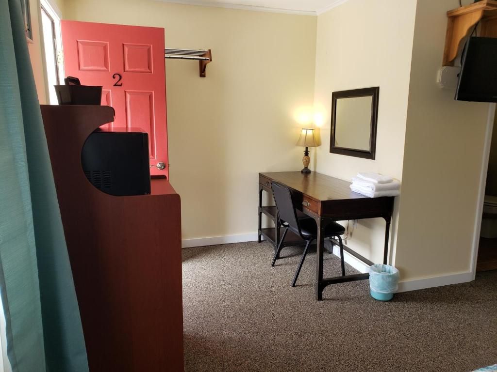 A hotel room with a desk, chair, a red door, a mirror, and a television.