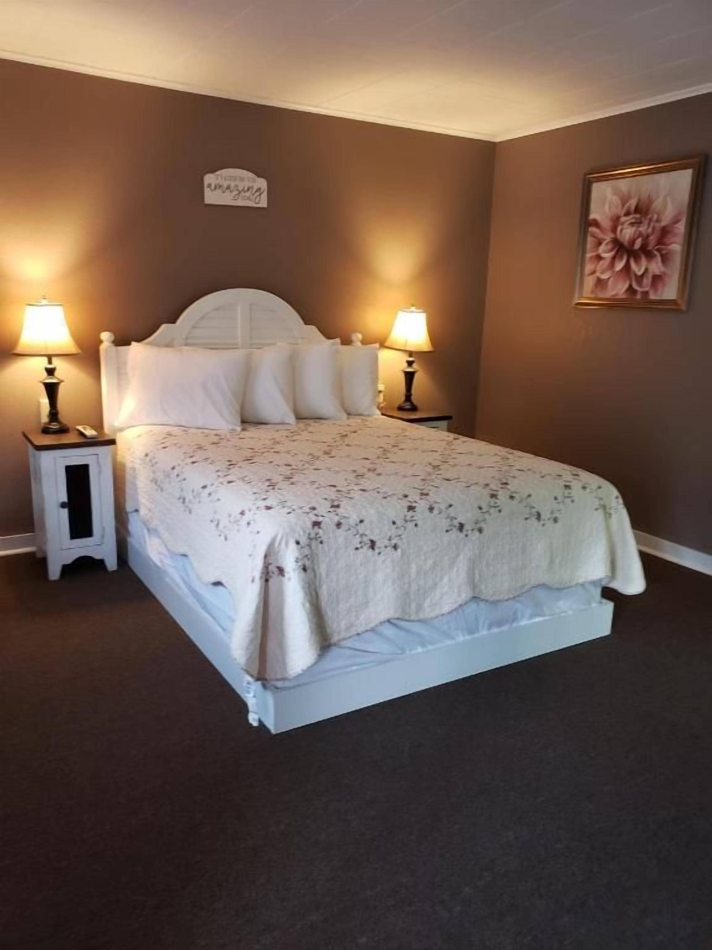A bedroom with a bed, two bedside tables, a nightstand, a wall-mounted sign, and a framed picture.