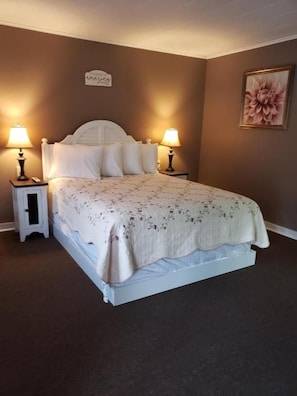 A bedroom with a bed, two bedside tables, a nightstand, a wall-mounted sign, and a framed picture. - Blue Ridge Motel (Schroon Lake)