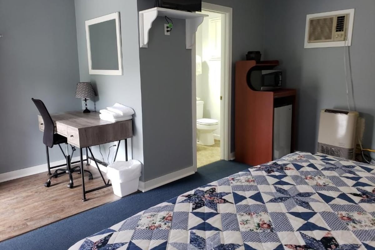 A bedroom with a bed, a desk, a chair, a microwave, and a television.