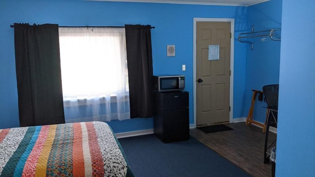 A room with a bed, a desk with a computer, a door, and a window with curtains.