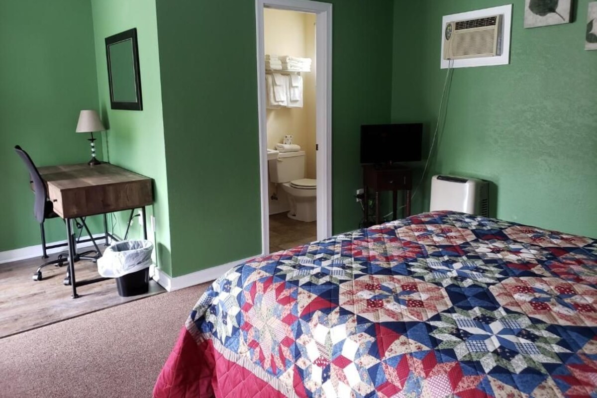 A room with a bed, a desk, a chair, a trash bin, and a television.