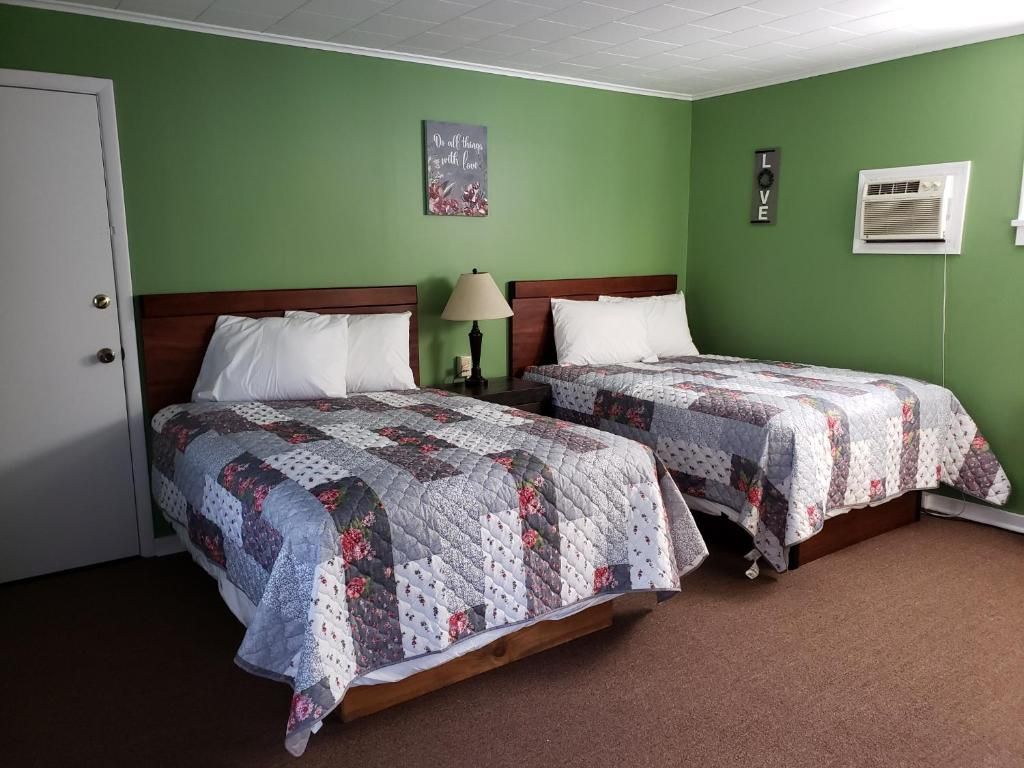 A room with two beds, a door, a wall-mounted air conditioner, and a wall decoration.