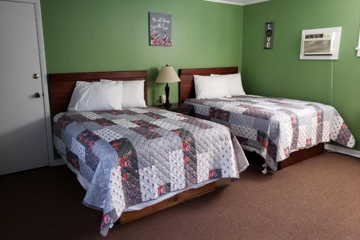 A room with two beds, a door, a wall-mounted air conditioner, and a wall decoration.