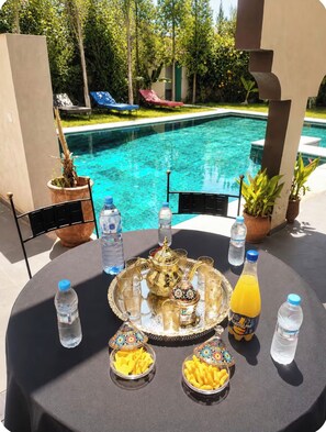 A poolside table with a tray of food, water bottles, and a teapot. - New Listing (Dar El Hamra)