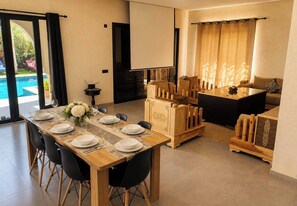 A dining area with a wooden table set for four, a sofa, and a TV screen. - New Listing (Dar El Hamra)