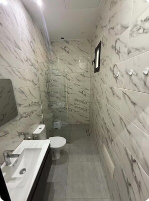 A bathroom with a marble wall, a toilet, a sink, and a shower area. - New Listing (Dar El Hamra)
