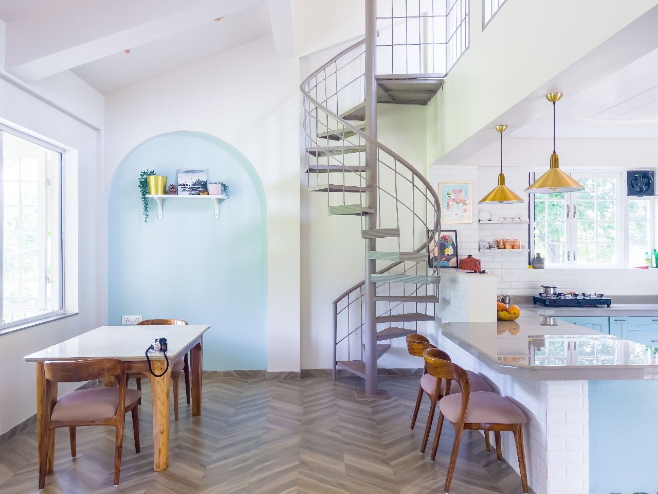Una cucina moderna con isola centrale, un'area pranzo con tavolo e sedie in legno e una scala a chiocciola che collega a un piano superiore.