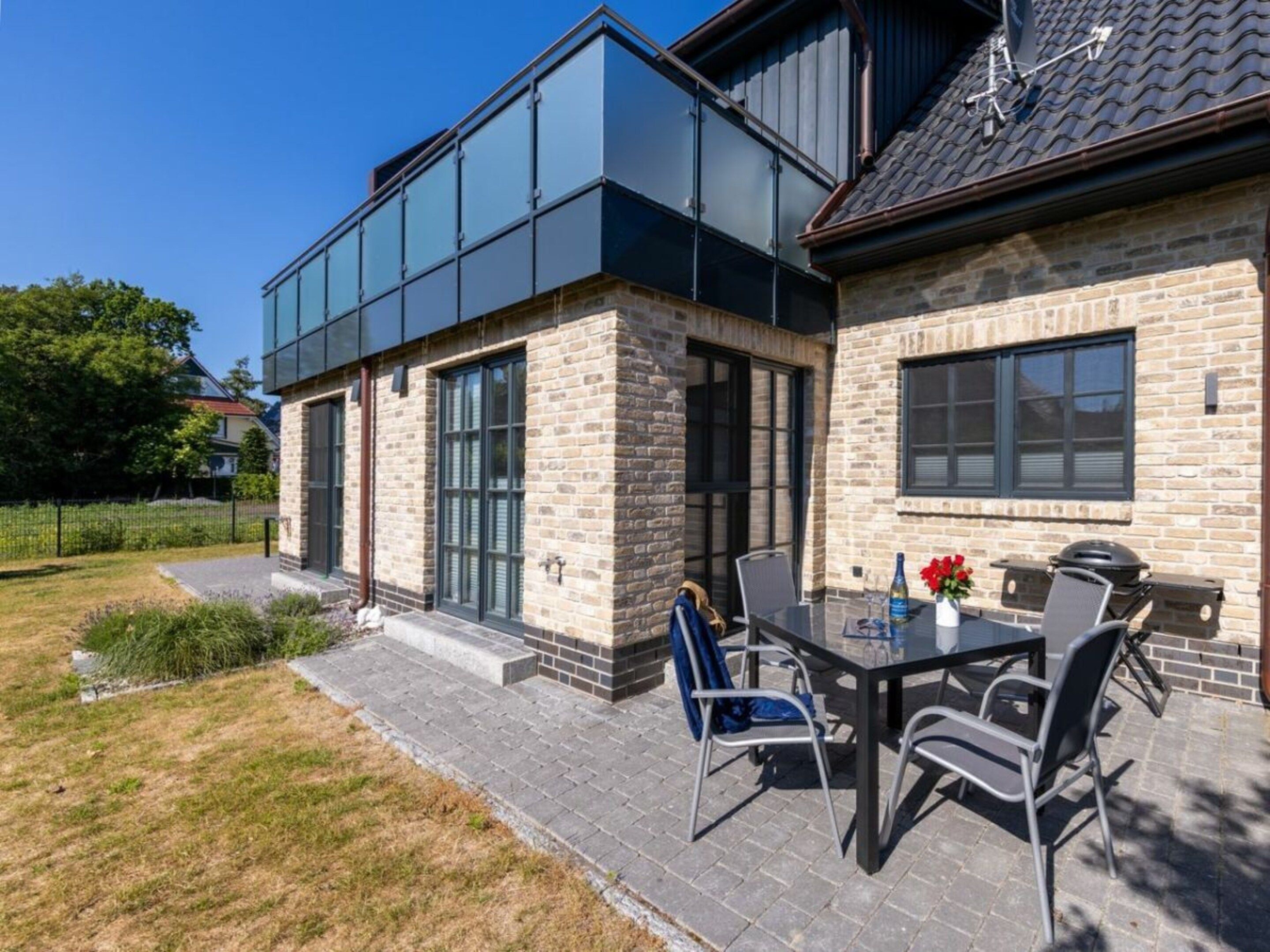 A modern house with a patio featuring a table and chairs, a barbecue grill, and a garden area.