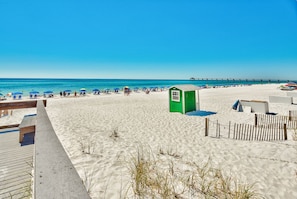 A beach with a wooden boardwalk, a green structure, and a pier in the distance. - Bayfront Paradise! Lazy River, Beach Access & Private Patio! (Fort Walton Beach)