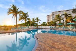 A swimming pool with lounge chairs and palm trees, surrounded by a building with multiple floors. - Bright Beachfront Penthouse | Balcony Views + Pool (Treasure Island)