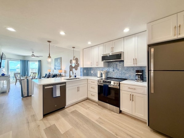 A modern kitchen with a central island, stainless steel appliances, and a view to the living area. - Bright Beachfront Penthouse | Balcony Views + Pool (Treasure Island)