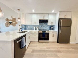 A modern kitchen with white cabinets, stainless steel appliances, and a blue tiled backsplash. - Bright Beachfront Penthouse | Balcony Views + Pool (Treasure Island)