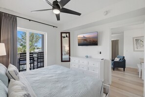 Une chambre à coucher comprenant un lit, un téléviseur, un ventilateur de plafond, une commode et une vue sur l’extérieur.