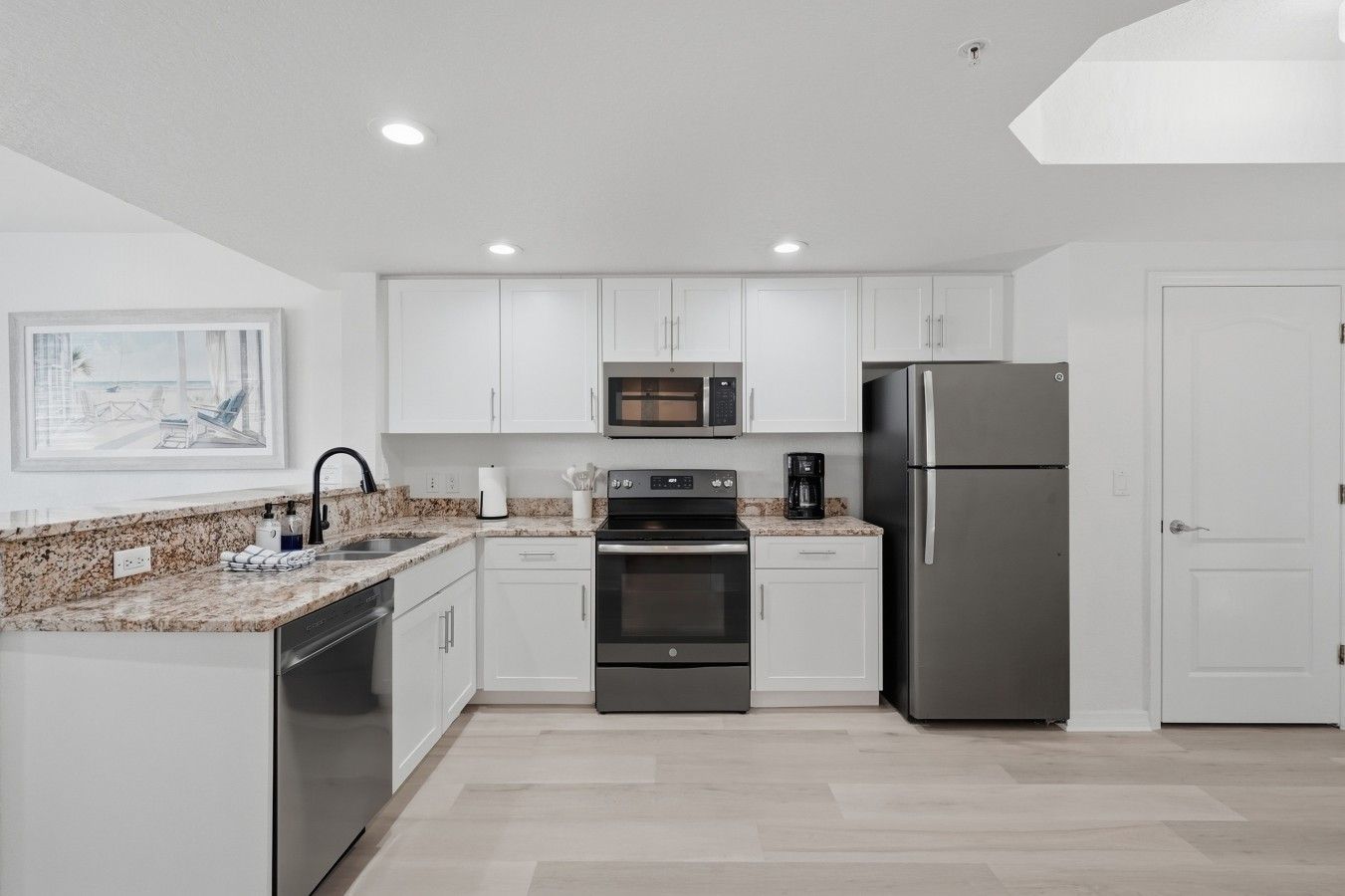 A modern kitchen with white cabinets, a stainless steel refrigerator, a microwave, and an oven.