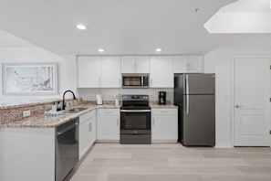 A modern kitchen with white cabinets, a stainless steel refrigerator, a microwave, and an oven. - Beachfront Escape Sunset Vista Resort Views & Pool (Treasure Island)