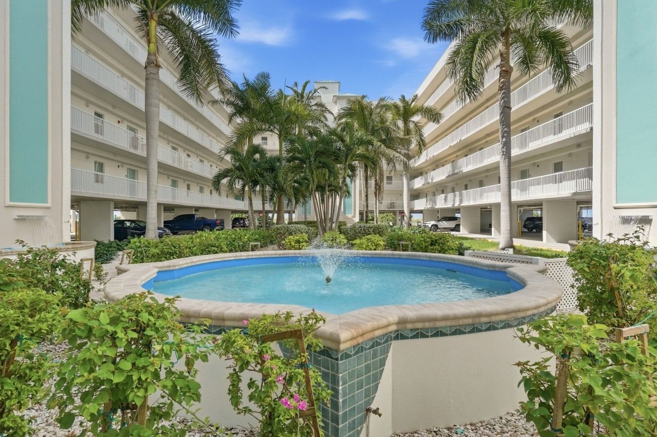 A hotel courtyard with a central pool, surrounded by palm trees and a multi-story building with balconies.