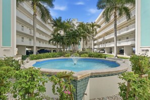 A hotel courtyard with a central pool, surrounded by palm trees and a multi-story building with balconies. - Beachfront Escape Sunset Vista Resort Views & Pool (Treasure Island)