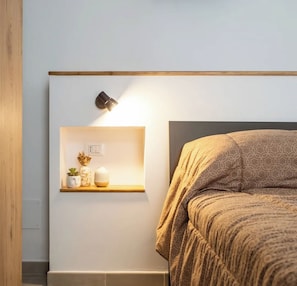 Ein Schlafzimmer mit einem Bett, einem Nachttisch mit Lampe und einem Regal mit Dekoration.