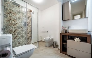 A bathroom with a shower, toilet, bidet, and a vanity with a mirror and towel storage. - New Listing (Palermo)