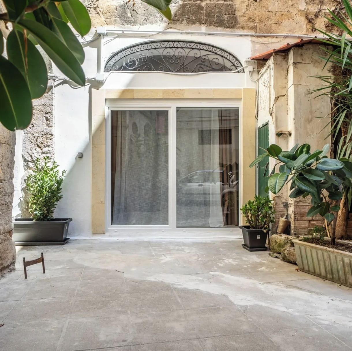 A courtyard with a white door, potted plants, and a stone wall.