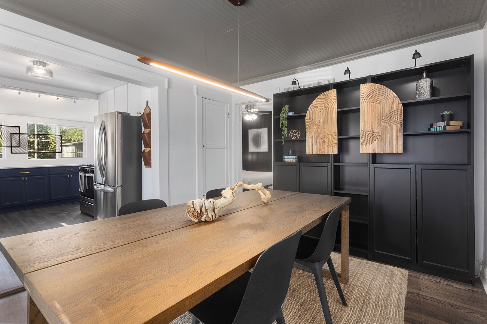 Une cuisine moderne avec une table à manger en bois, des meubles de rangement noirs et un luminaire suspendu.