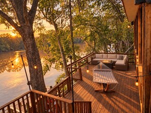 A wooden deck with a sofa and a hammock, overlooking a body of water.