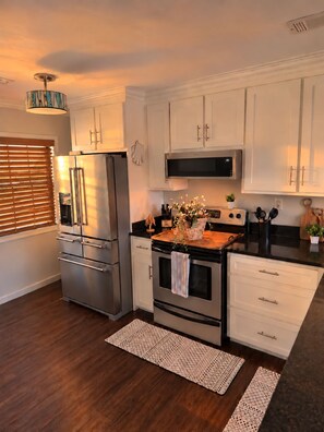 A modern kitchen with stainless steel appliances, white cabinetry, and a wooden countertop.