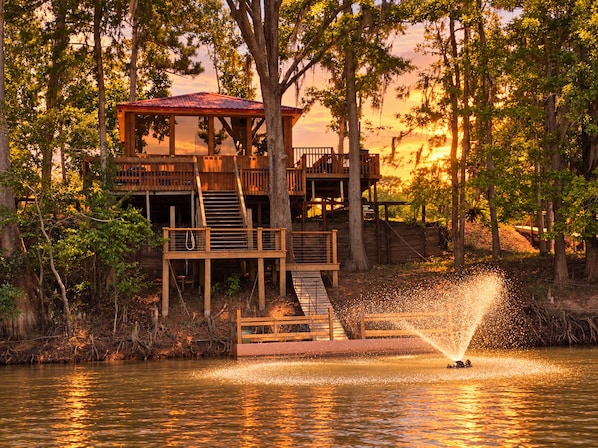 A wooden cabin with a red roof, surrounded by trees and a body of water.