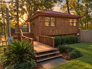 A wooden cabin with a red roof, a wooden deck, and a staircase leading to the entrance.