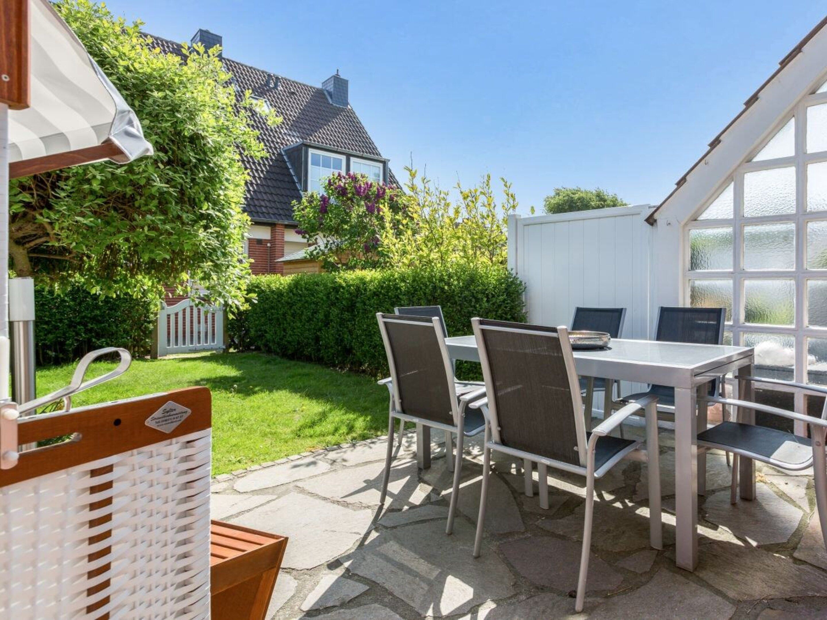 An outdoor patio with a table and chairs, a grill, and a view of a house and garden.