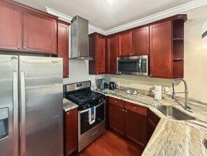 A kitchen with stainless steel appliances, wooden cabinets, a microwave, and a sink. - Cozy Urban Studio | Fitness Hub | Perfect For 2 (Philadelphia)
