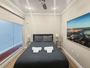 A hotel room with a bed, two bedside lamps, a ceiling fan, a large window, and a painting of a landscape. - Sleek City Flat 1BR | Culinary Hub | Ideal for 2 (Philadelphia)