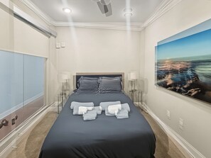 A hotel room with a large bed, two bedside lamps, a painting of a beach, and a wardrobe. - Sleek City Flat 1BR | Culinary Hub | Ideal for 2 (Philadelphia)